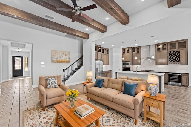 tiled living room with ceiling fan, wet bar, beverage cooler, and beamed ceiling