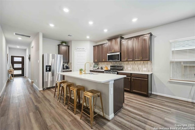 kitchen featuring sink, appliances with stainless steel finishes, a kitchen breakfast bar, an island with sink, and decorative backsplash