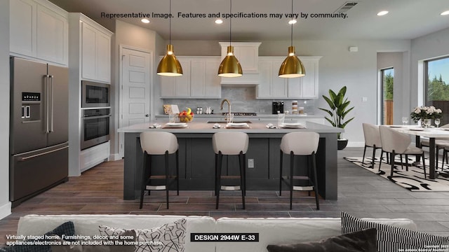 kitchen with hanging light fixtures, appliances with stainless steel finishes, a kitchen island with sink, and white cabinets