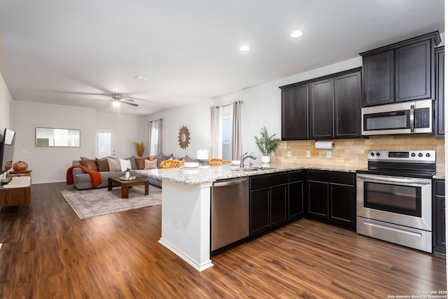 kitchen with dark wood-type flooring, sink, appliances with stainless steel finishes, kitchen peninsula, and decorative backsplash