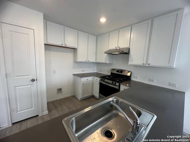 kitchen featuring white cabinetry, stainless steel range with gas cooktop, dark hardwood / wood-style floors, and sink