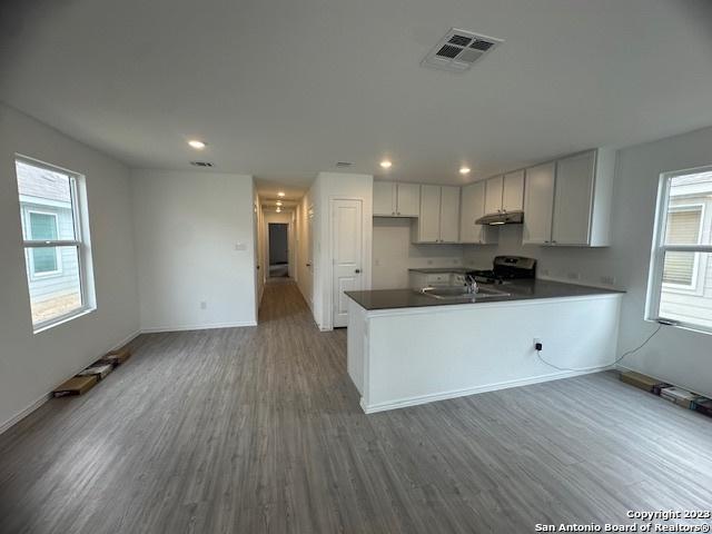 kitchen with dark wood-type flooring, sink, white cabinetry, kitchen peninsula, and stove