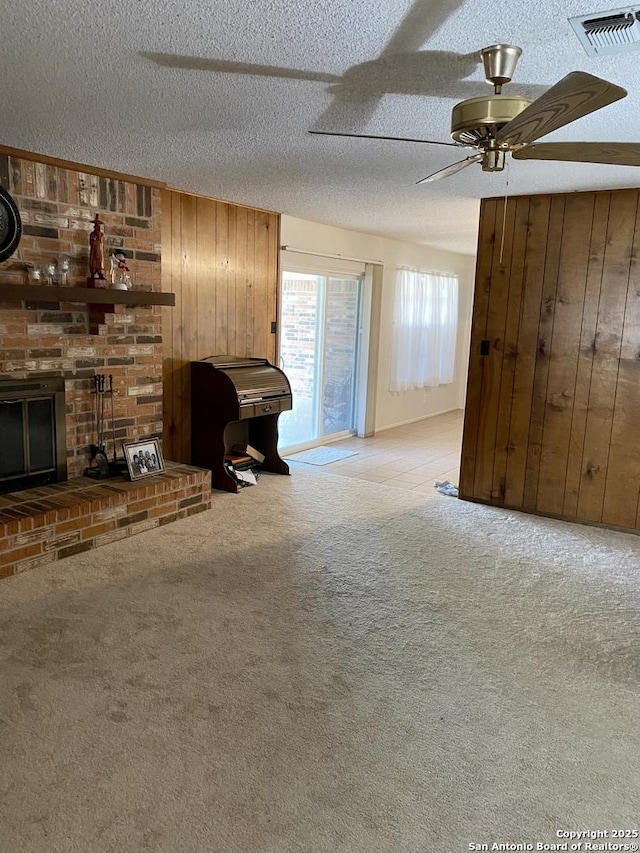 unfurnished living room with a fireplace, wood walls, ceiling fan, light carpet, and a textured ceiling