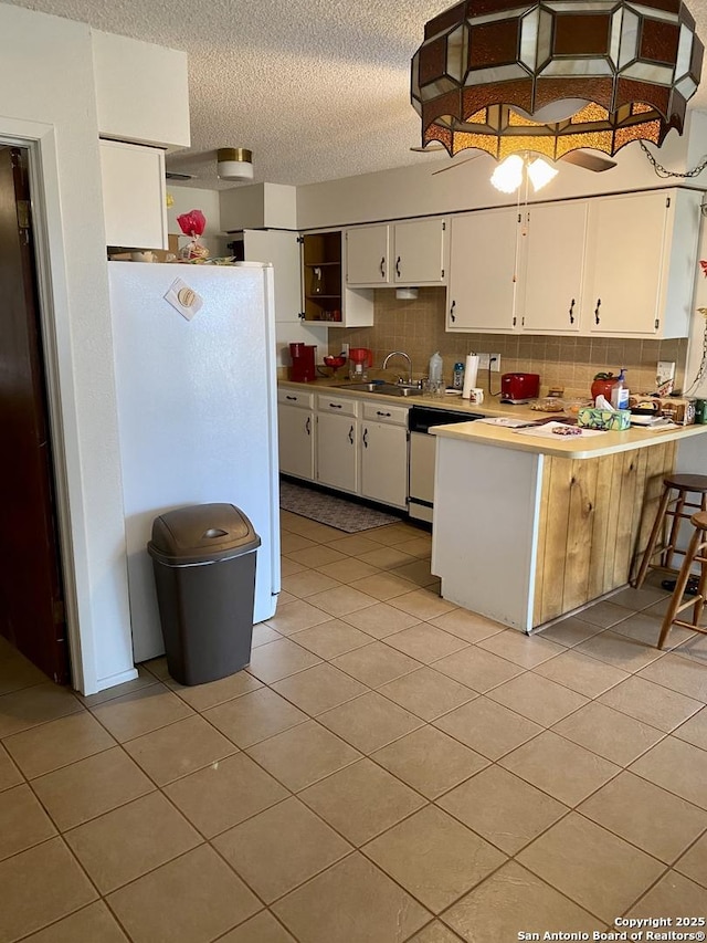 kitchen featuring tasteful backsplash, a textured ceiling, stainless steel dishwasher, white fridge, and white cabinets