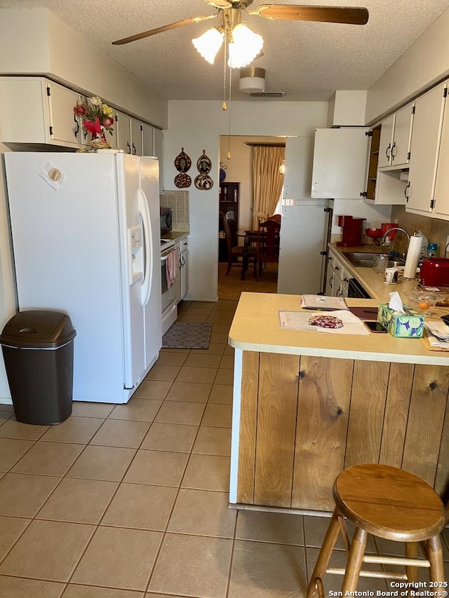 kitchen featuring light tile patterned floors, white appliances, kitchen peninsula, and white cabinets