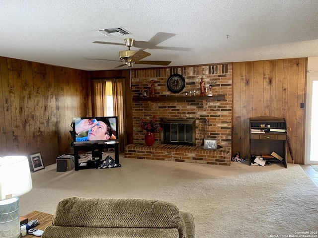 living room with a brick fireplace, light colored carpet, a textured ceiling, and wood walls