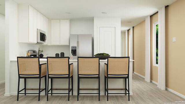 kitchen with stainless steel appliances, a breakfast bar, light hardwood / wood-style floors, and white cabinets