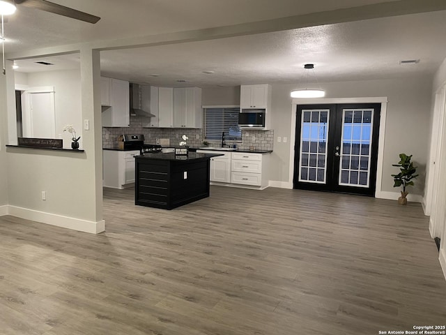 kitchen featuring wall chimney range hood, hardwood / wood-style flooring, stainless steel appliances, white cabinets, and french doors