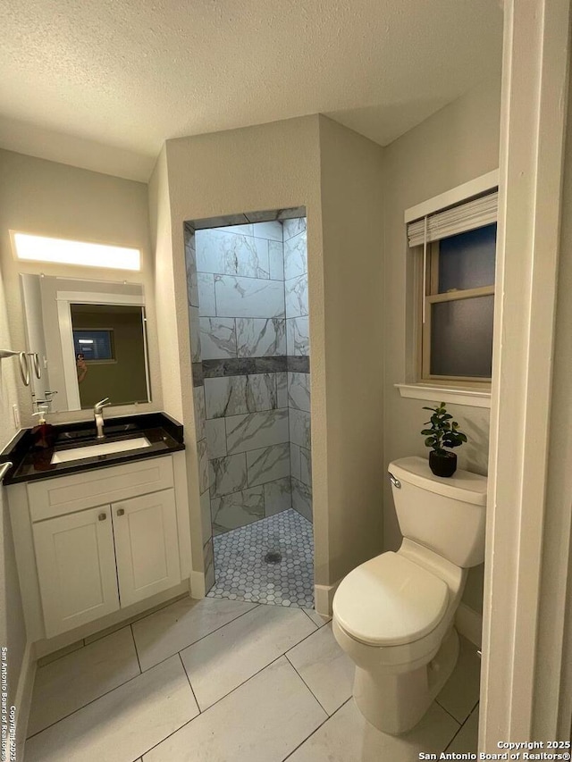 bathroom with tile patterned floors, toilet, a textured ceiling, a tile shower, and vanity