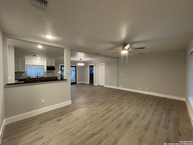 unfurnished living room with hardwood / wood-style flooring, ceiling fan, and sink