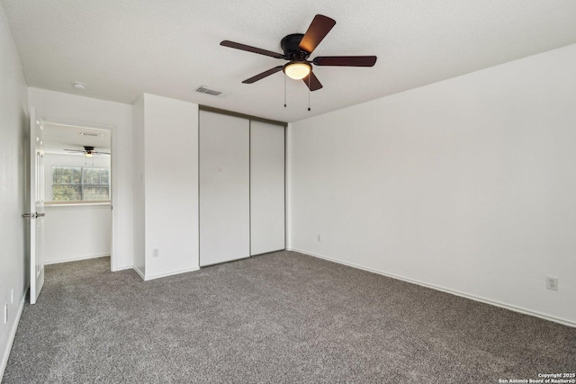 unfurnished bedroom with ceiling fan, a closet, a textured ceiling, and dark colored carpet