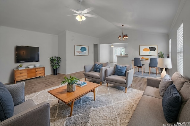 living room featuring vaulted ceiling, ornamental molding, ceiling fan with notable chandelier, and light wood-type flooring