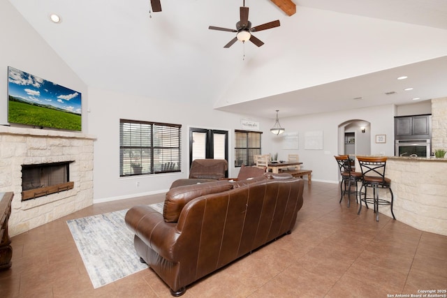 tiled living room with ceiling fan, high vaulted ceiling, and a fireplace