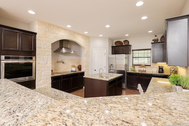 kitchen featuring a kitchen island, tasteful backsplash, light stone counters, stainless steel appliances, and wall chimney range hood