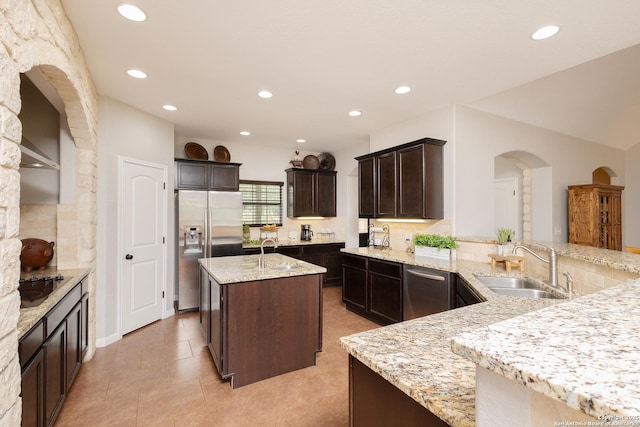 kitchen featuring sink, appliances with stainless steel finishes, a kitchen island with sink, light stone countertops, and kitchen peninsula