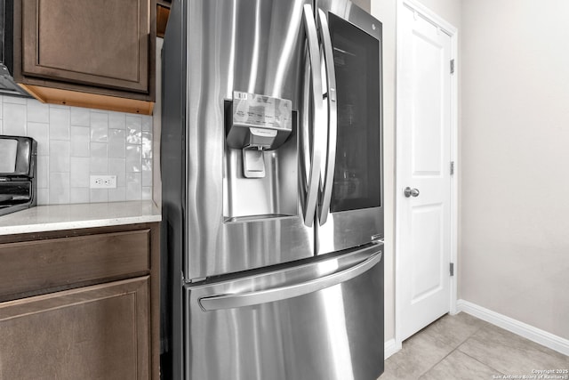 kitchen featuring stainless steel fridge, light tile patterned floors, dark brown cabinets, and backsplash