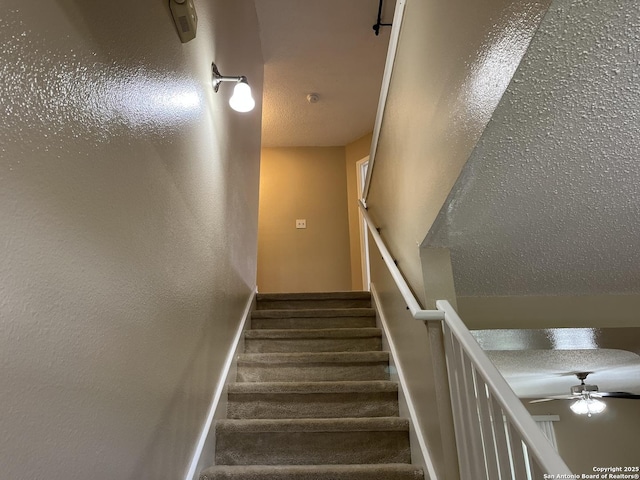 stairway featuring ceiling fan and a textured ceiling