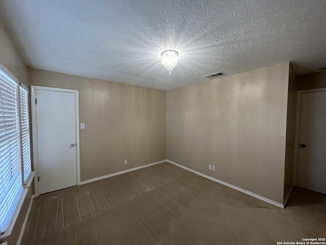 spare room featuring dark colored carpet and a textured ceiling