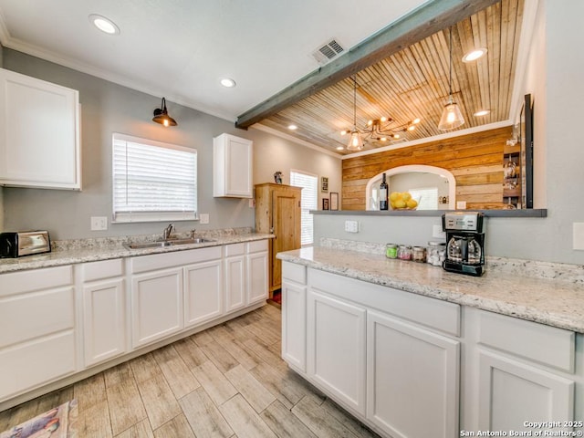 kitchen with sink, hanging light fixtures, ornamental molding, light hardwood / wood-style floors, and white cabinets