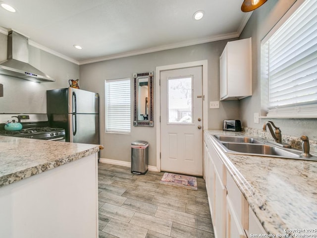 kitchen with appliances with stainless steel finishes, sink, white cabinets, ornamental molding, and wall chimney range hood