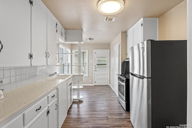 kitchen featuring dark hardwood / wood-style floors, sink, white cabinets, tile counters, and stainless steel appliances