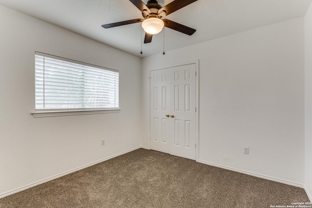 unfurnished bedroom with ceiling fan, dark carpet, and a closet