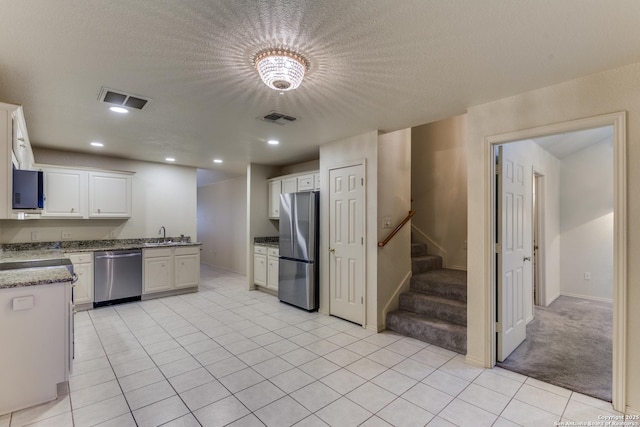 kitchen with light tile patterned flooring, sink, white cabinets, stainless steel appliances, and a textured ceiling