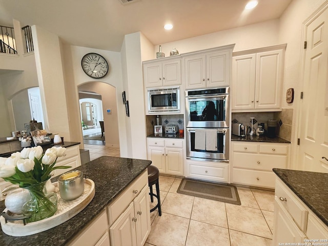 kitchen with tasteful backsplash, light tile patterned floors, dark stone counters, and appliances with stainless steel finishes