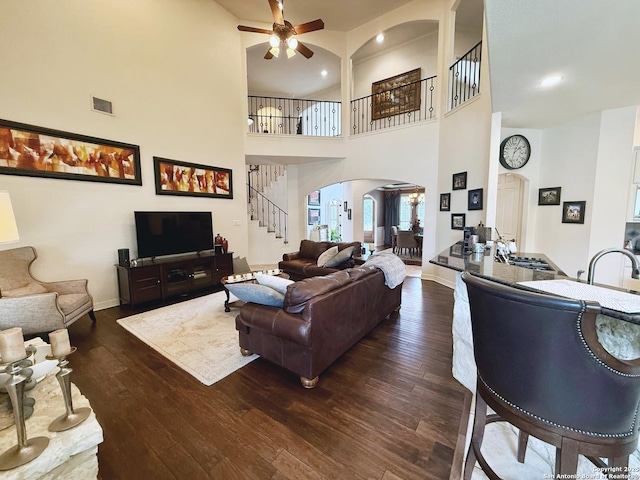 living room with dark hardwood / wood-style flooring, a towering ceiling, and ceiling fan