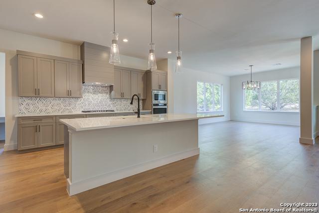 kitchen with tasteful backsplash, hanging light fixtures, light hardwood / wood-style flooring, appliances with stainless steel finishes, and a kitchen island with sink