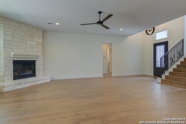 unfurnished living room with ceiling fan, a stone fireplace, and light wood-type flooring