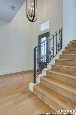 stairway with hardwood / wood-style flooring, a towering ceiling, and a chandelier