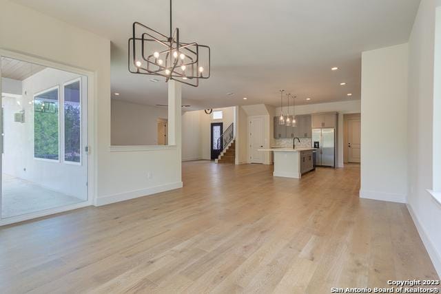 unfurnished living room with an inviting chandelier, sink, and light hardwood / wood-style flooring