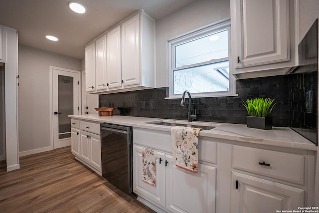 kitchen with hardwood / wood-style floors, white cabinetry, black dishwasher, sink, and light stone counters