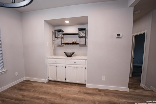 bar with white cabinets and light wood-type flooring