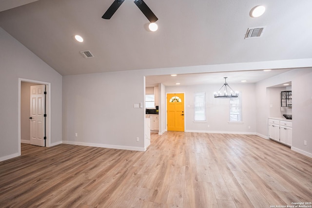 unfurnished living room with ceiling fan with notable chandelier, lofted ceiling, and light hardwood / wood-style floors