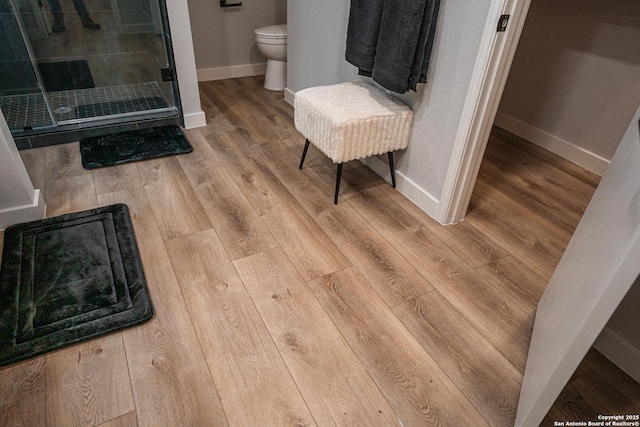 bathroom with hardwood / wood-style flooring, a shower with shower door, and toilet