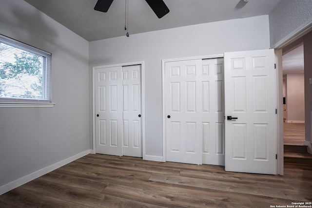 unfurnished bedroom featuring two closets, dark wood-type flooring, and ceiling fan