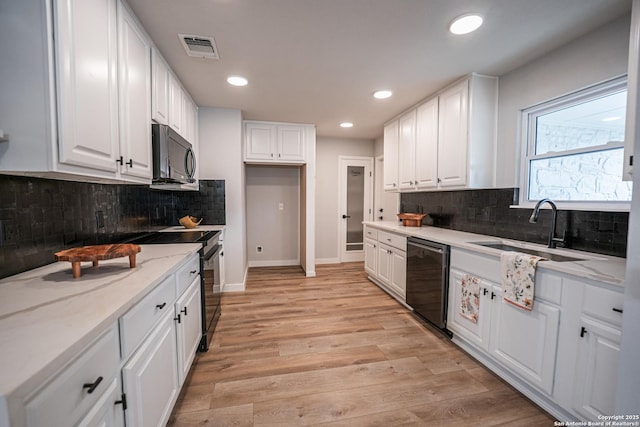 kitchen with sink, white cabinetry, black appliances, light stone countertops, and light wood-type flooring