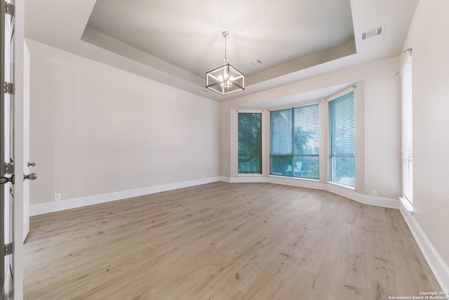 unfurnished room with a notable chandelier, light wood-type flooring, and a tray ceiling