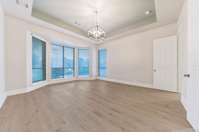 spare room featuring a notable chandelier, a tray ceiling, and light wood-type flooring