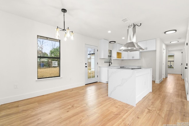 kitchen with pendant lighting, island range hood, white cabinetry, sink, and light stone counters