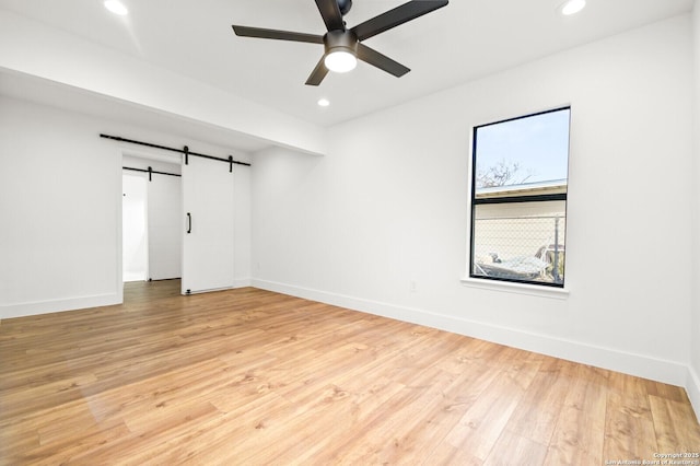 empty room featuring ceiling fan, a barn door, and light wood-type flooring