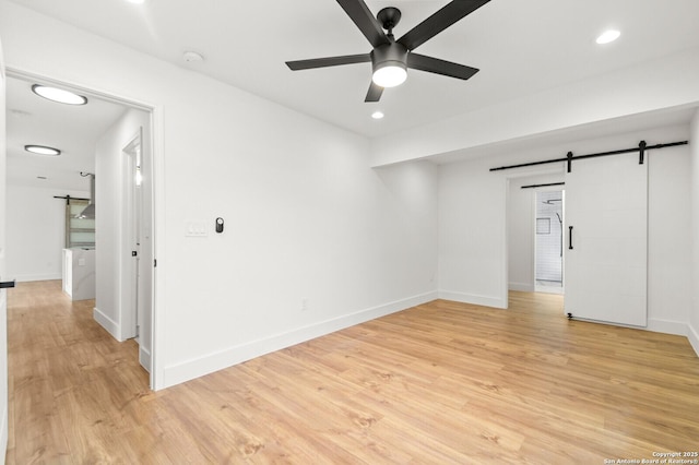 spare room featuring light hardwood / wood-style flooring, a barn door, and ceiling fan