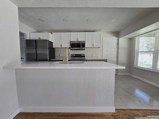 kitchen featuring sink, tasteful backsplash, appliances with stainless steel finishes, kitchen peninsula, and white cabinets