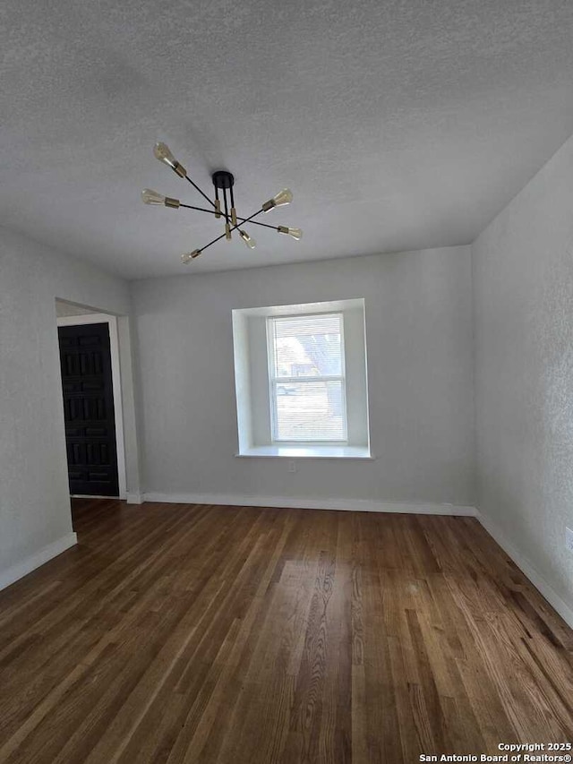 spare room with a notable chandelier, dark hardwood / wood-style floors, and a textured ceiling