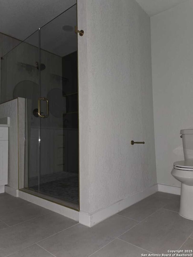 bathroom featuring tile patterned flooring, a shower with door, and toilet