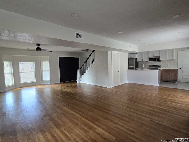 unfurnished living room featuring ceiling fan, dark wood-type flooring, sink, and a textured ceiling