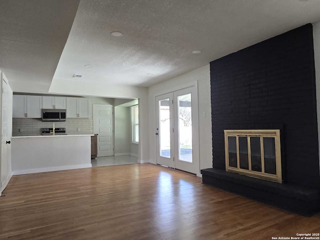 unfurnished living room featuring hardwood / wood-style flooring, a brick fireplace, and a textured ceiling