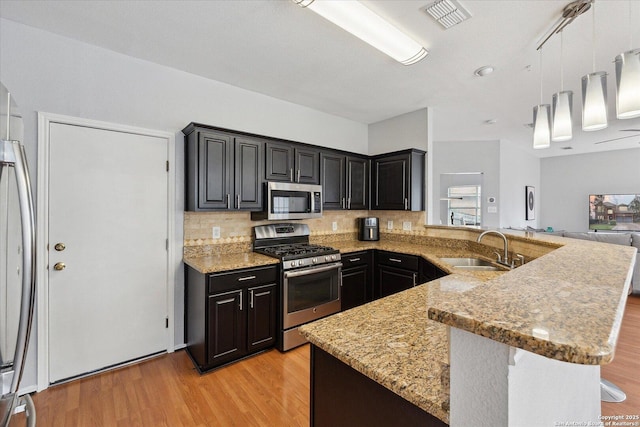 kitchen with sink, light hardwood / wood-style flooring, stainless steel appliances, decorative backsplash, and decorative light fixtures